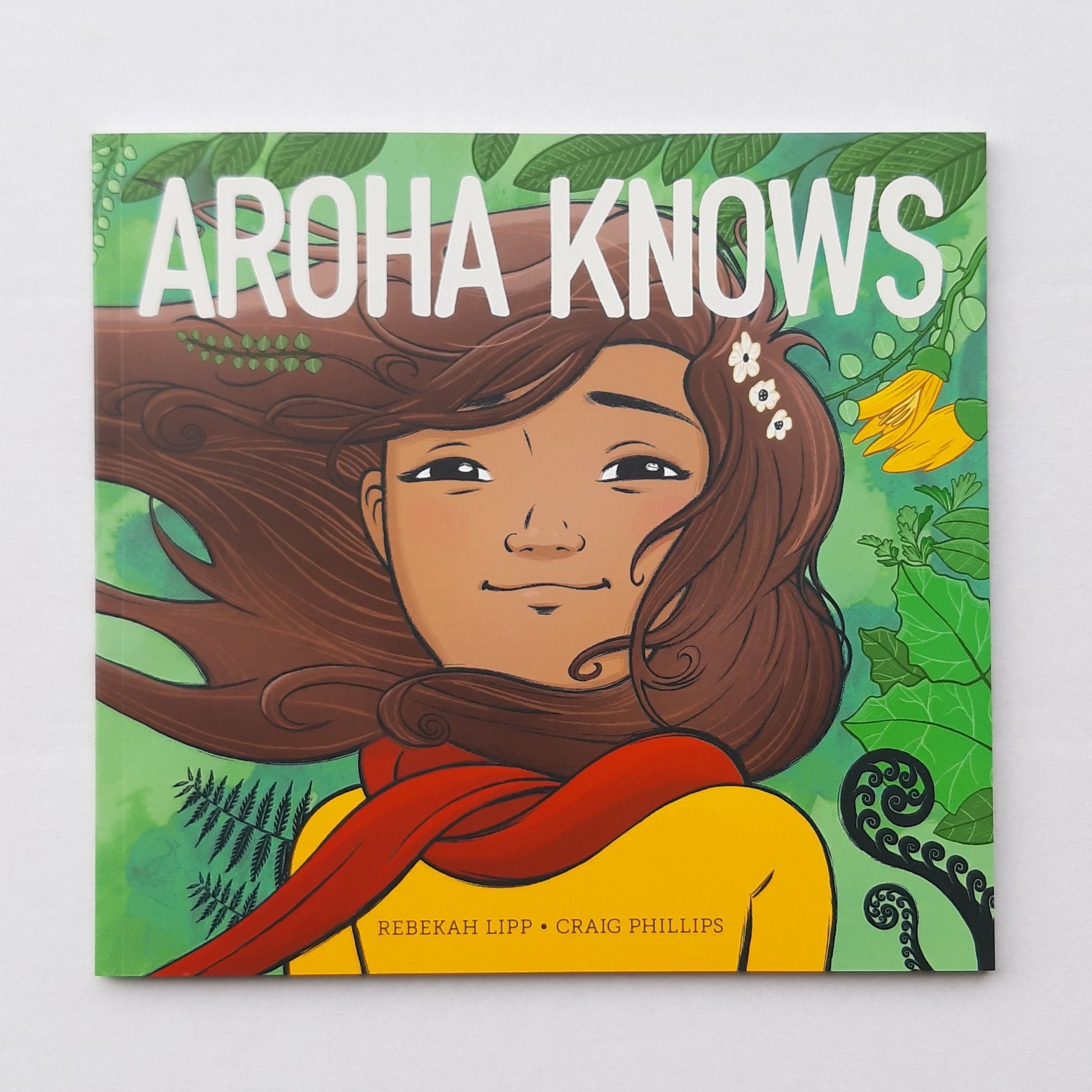 Aroha Knows book. Cover: A brown-haired girl standing in native bush, smiling contently. Wearing red scarf and yellow shirt.