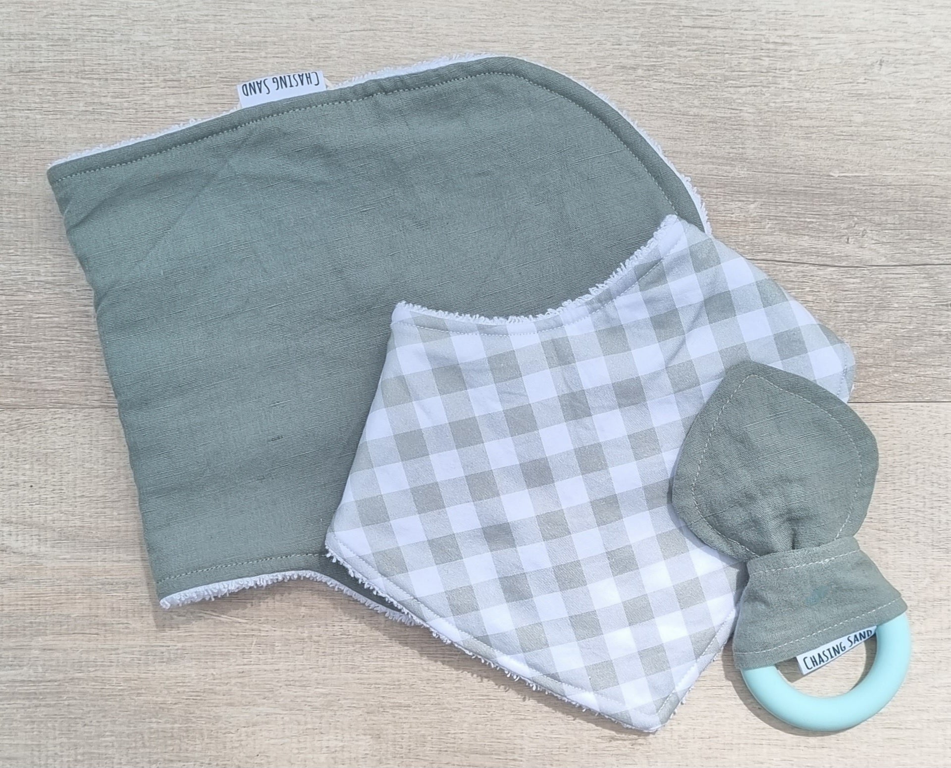 Sage green Gingham 3 Piece Gift Set against wooden backdrop. Matching Burp Cloth, Dribble Bib and Teether.