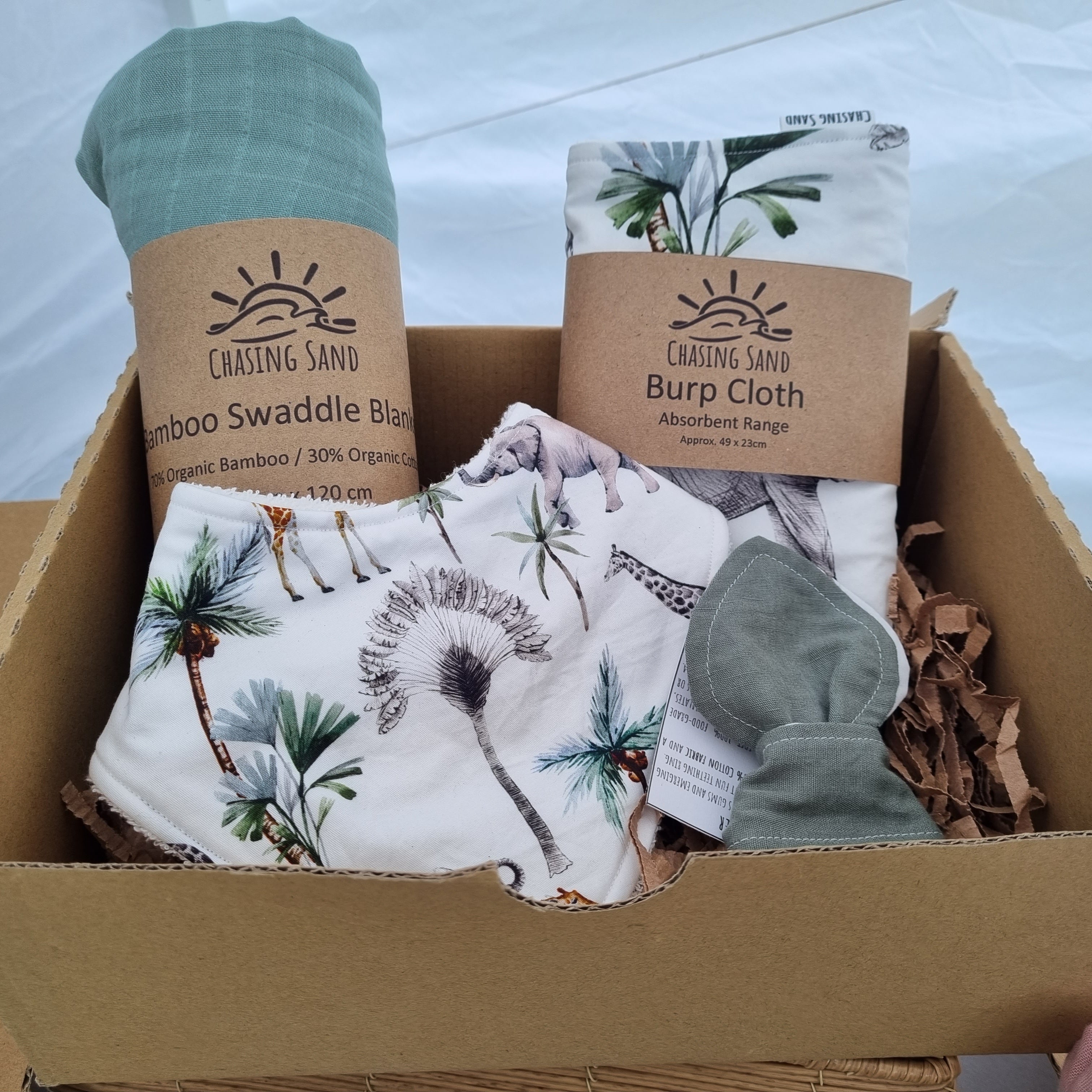 Chasing Sand Gift Box, containing 1x Swaddle in a green colour, 1x Burp Cloth in Safari, 1x Dribble Bib in Safari and 1x Teether in a dark green colour.