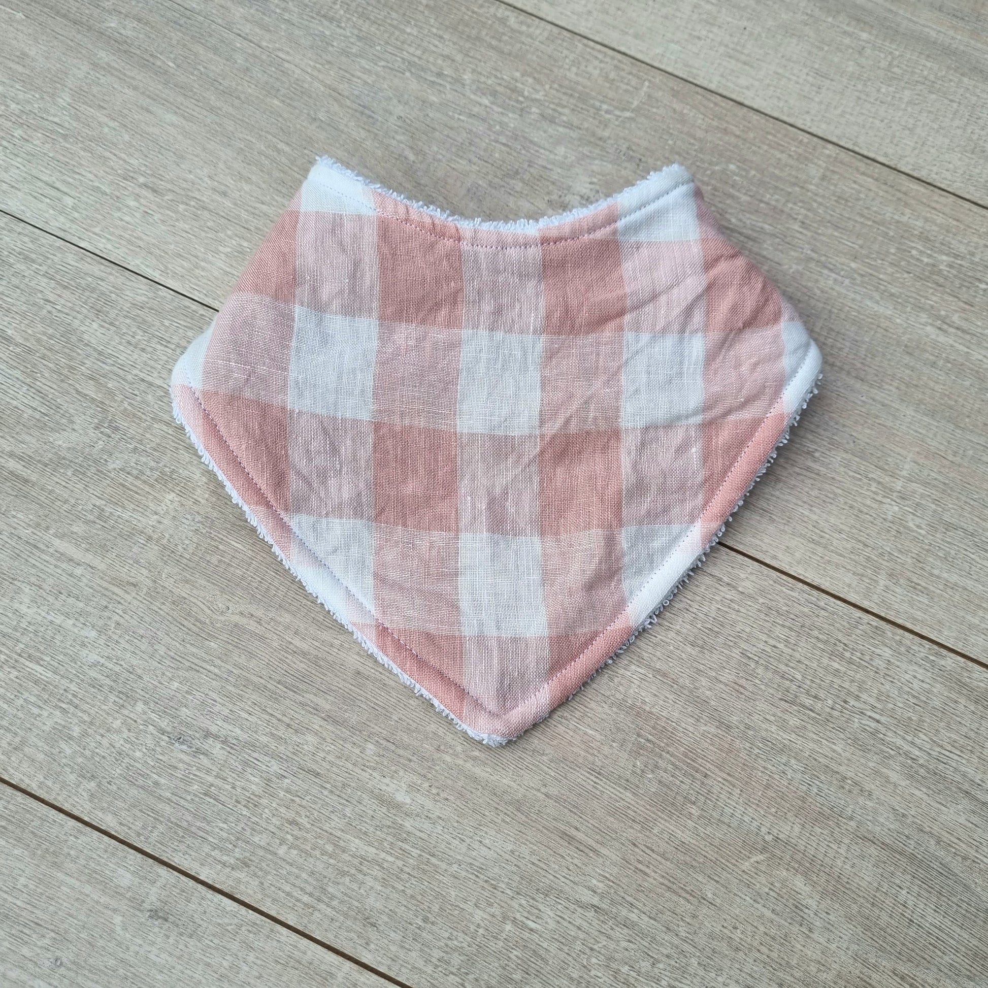 Dribble Bib - Pink Gingham Linen against wooden backdrop. Soft pastel pink checkered pattern on white background