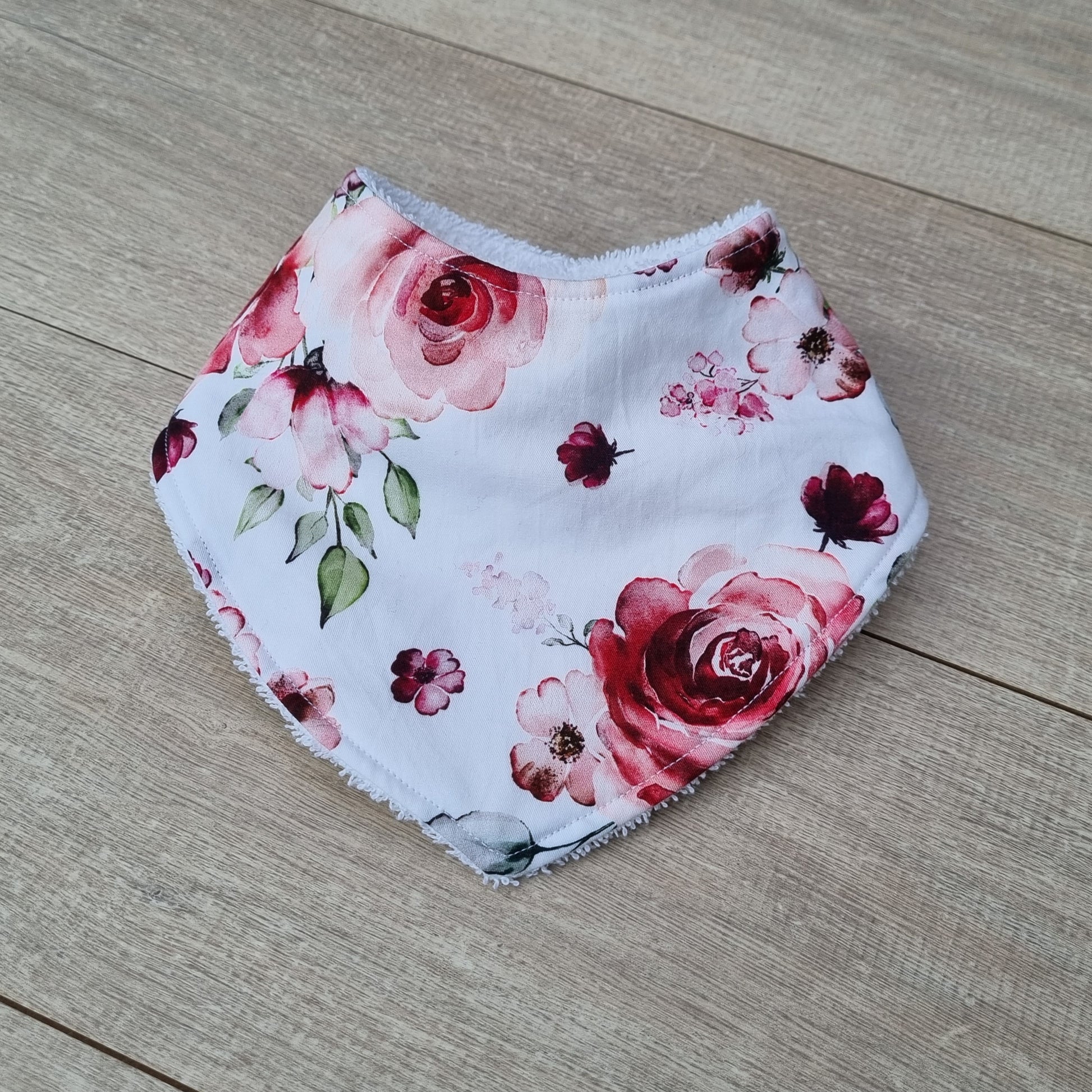 Dribble Bib - Rose Garden against wooden backdrop. Pink watercolour rose design with green leaves on white background.