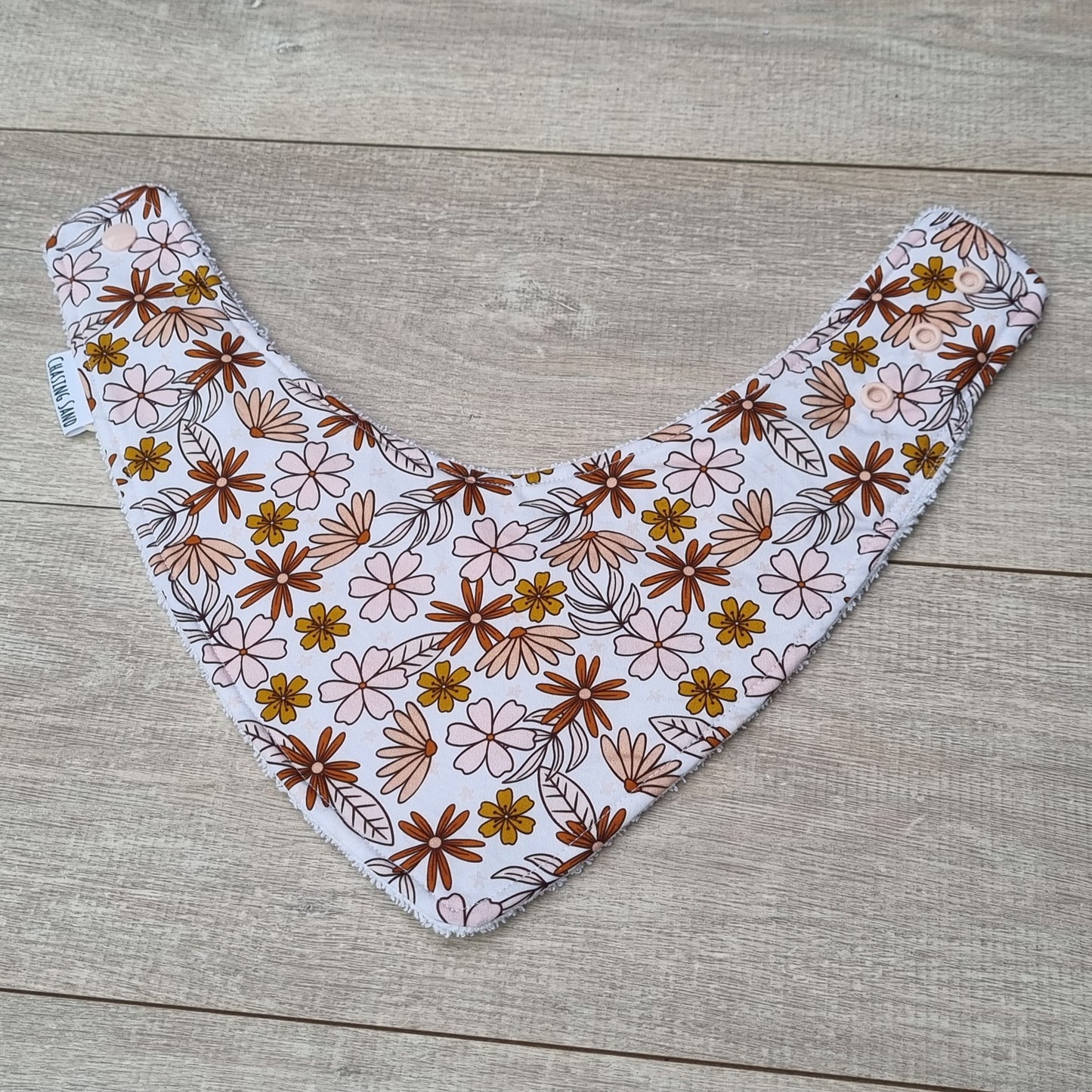 Dribble Bib - Willow against wooden backdrop. Brown and pink flowers on white background.