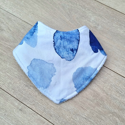 Dribble Bib - Watercolour against wooden backdrop. Blue watercolour patches on white background.