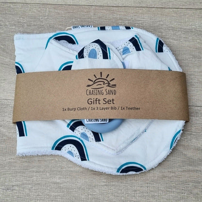 3 Piece Gift Set - Blue Rainbows against wooden backdrop. Blue rainbow design on white background. Each set contains 1x Burp Cloth, 1x Dribble Bib and 1x Teether.