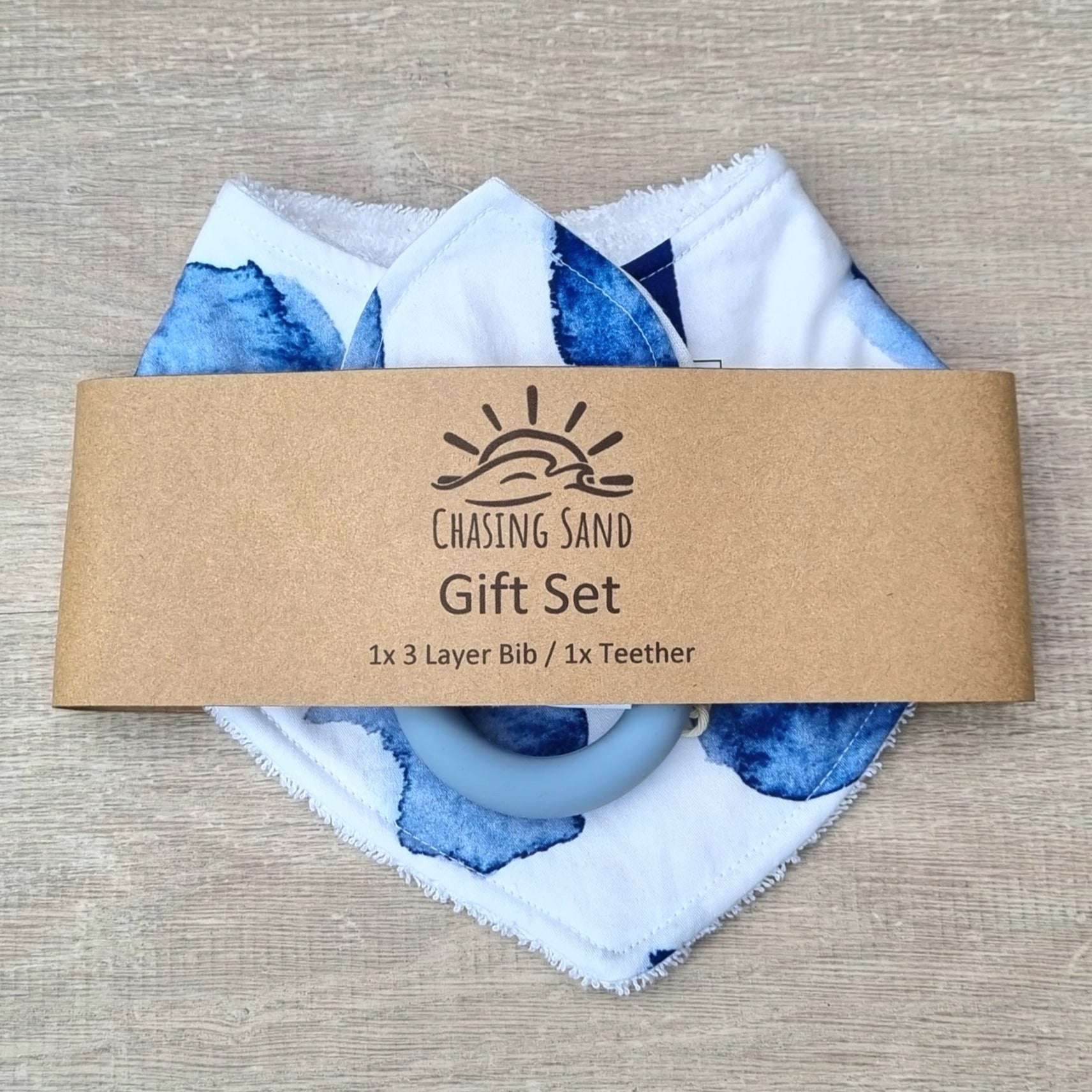 2 Piece Gift Set - Watercolour against wooden backdrop. Blue watercolour patches on white background. Each set contains 1x Dribble Bib and 1x Teether.