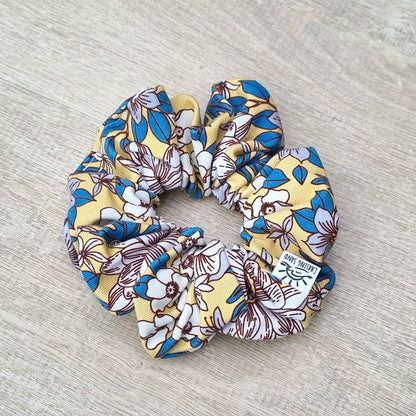 Scrunchie - April against wooden backdrop. Blue and white flowers on yellow background.