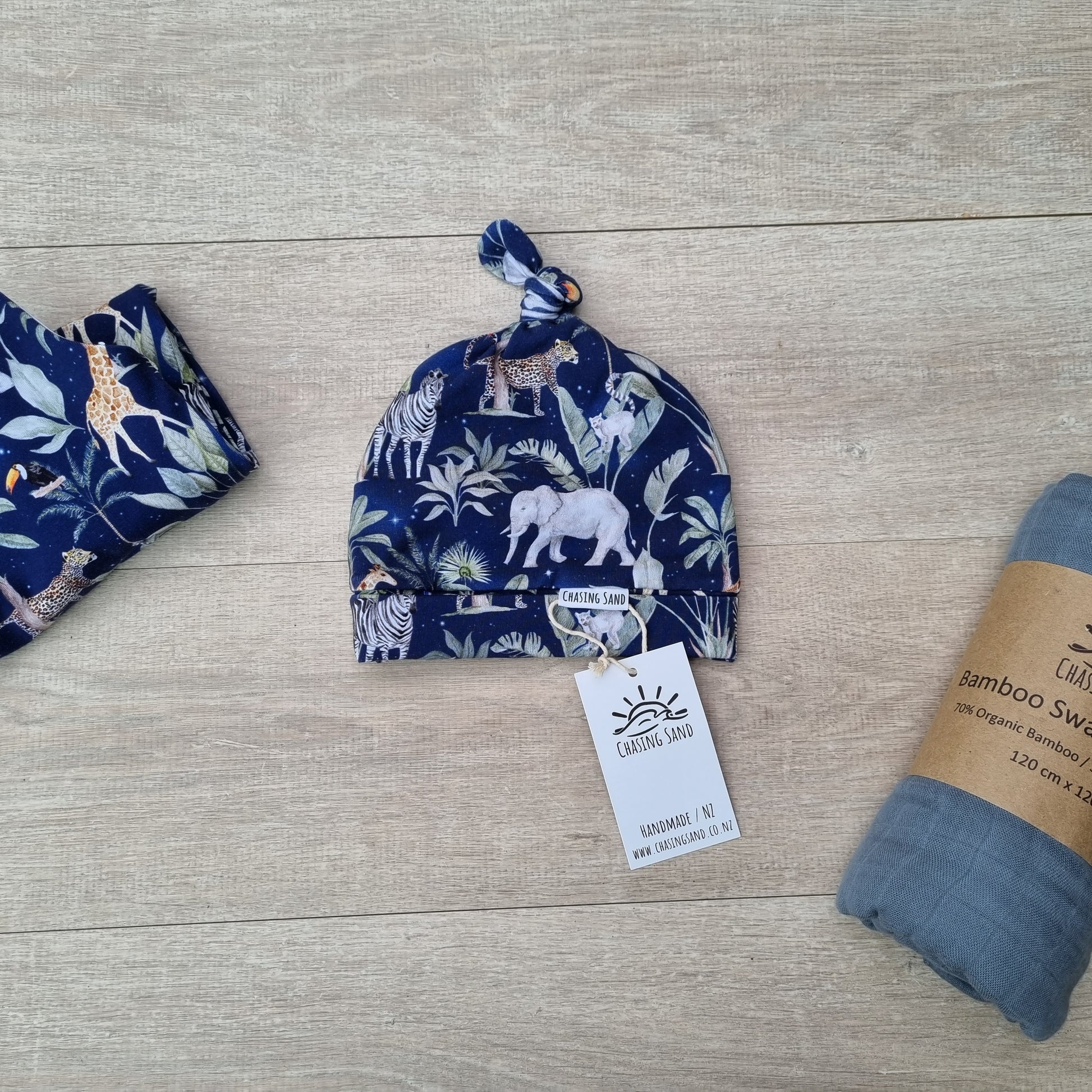 Beanie - Night Safari against wooden backdrop. African animal and plant illustrations against navy blue background.