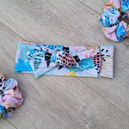 Top Knot Headband - Dana against wooden backdrop. Pink, yellow, black and blue abstract pattern.