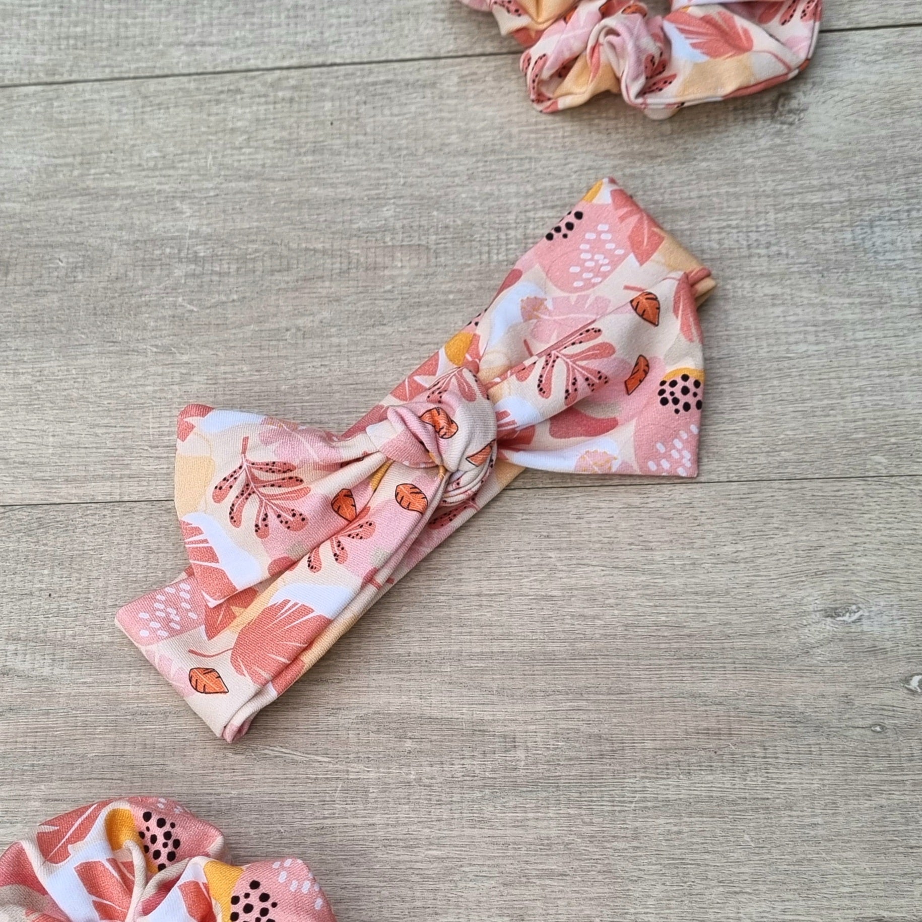 Top Knot Headband - Sara against wooden backdrop. Pink and orange leaves on white background.