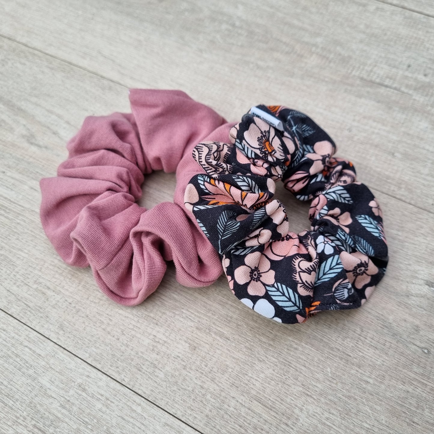 Scrunchie - Florence against wooden backdrop. Orange and pink flowers with leaves on black background.