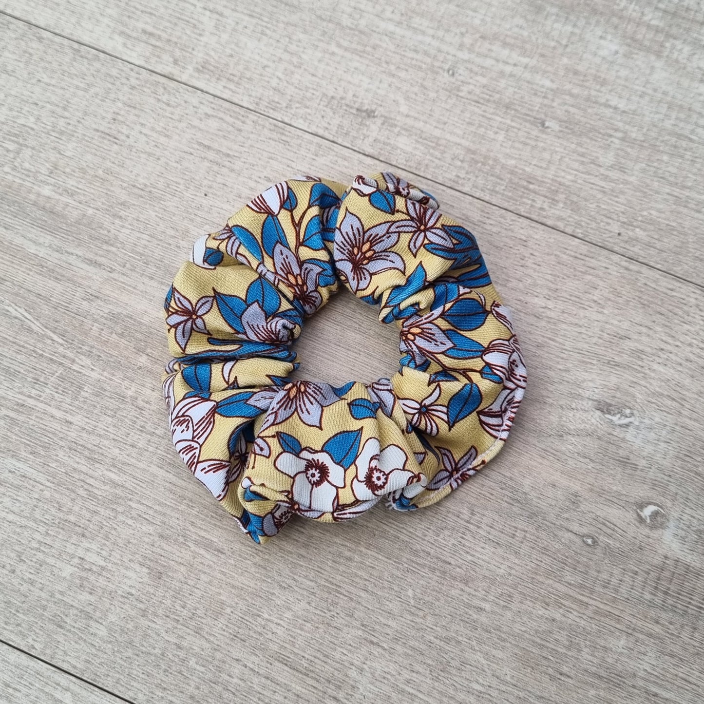 Scrunchie - April against wooden backdrop. Blue and white flowers on yellow background.