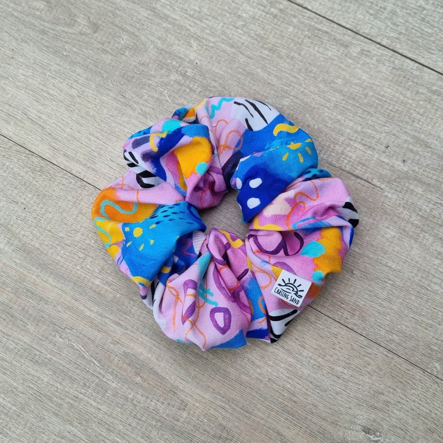 Scrunchie - Swirls against wooden backdrop. Blue, orange and purple abstract pattern on pink background.