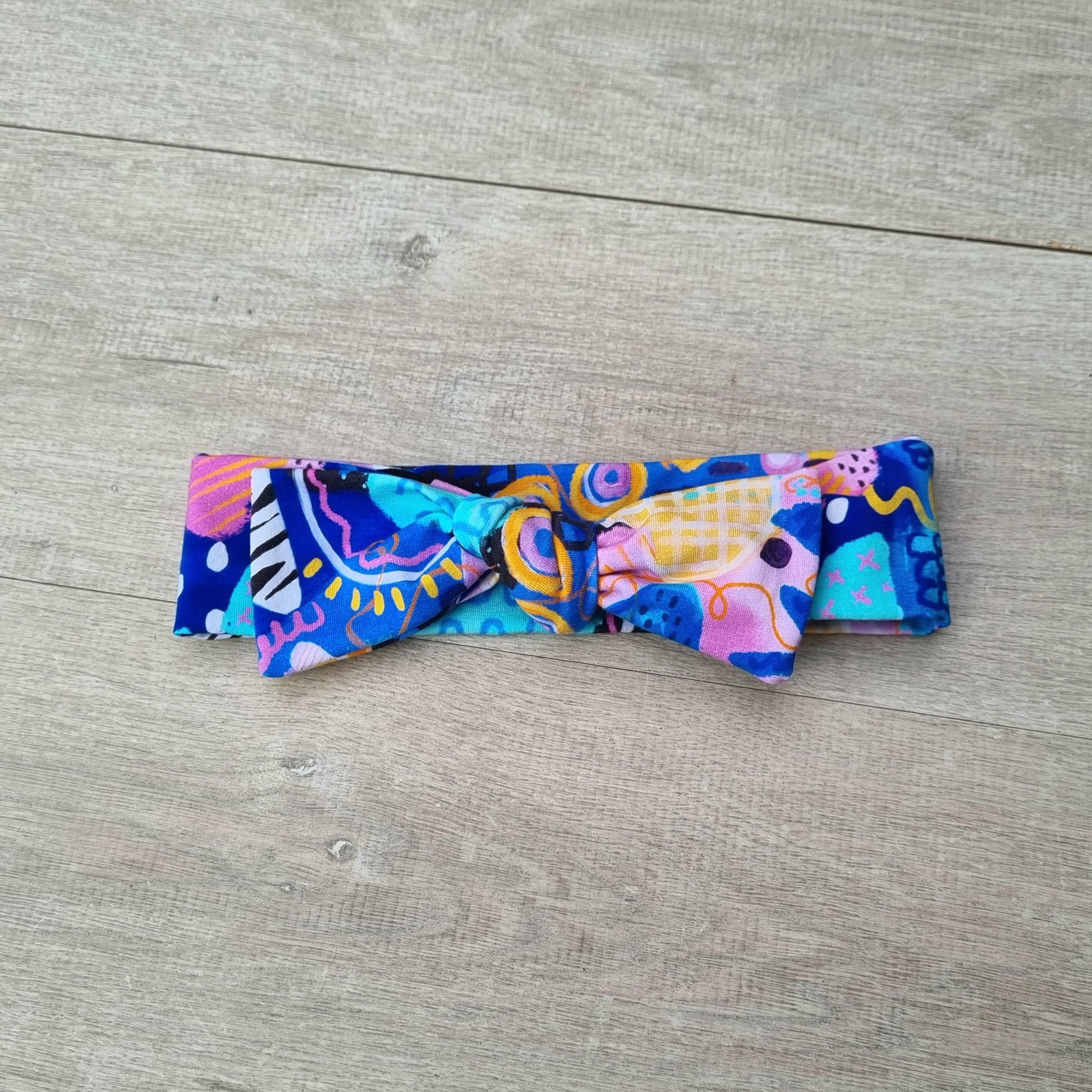 Top Knot Headband - Swirls against wooden backdrop. Blue, orange and purple abstract pattern on pink background.