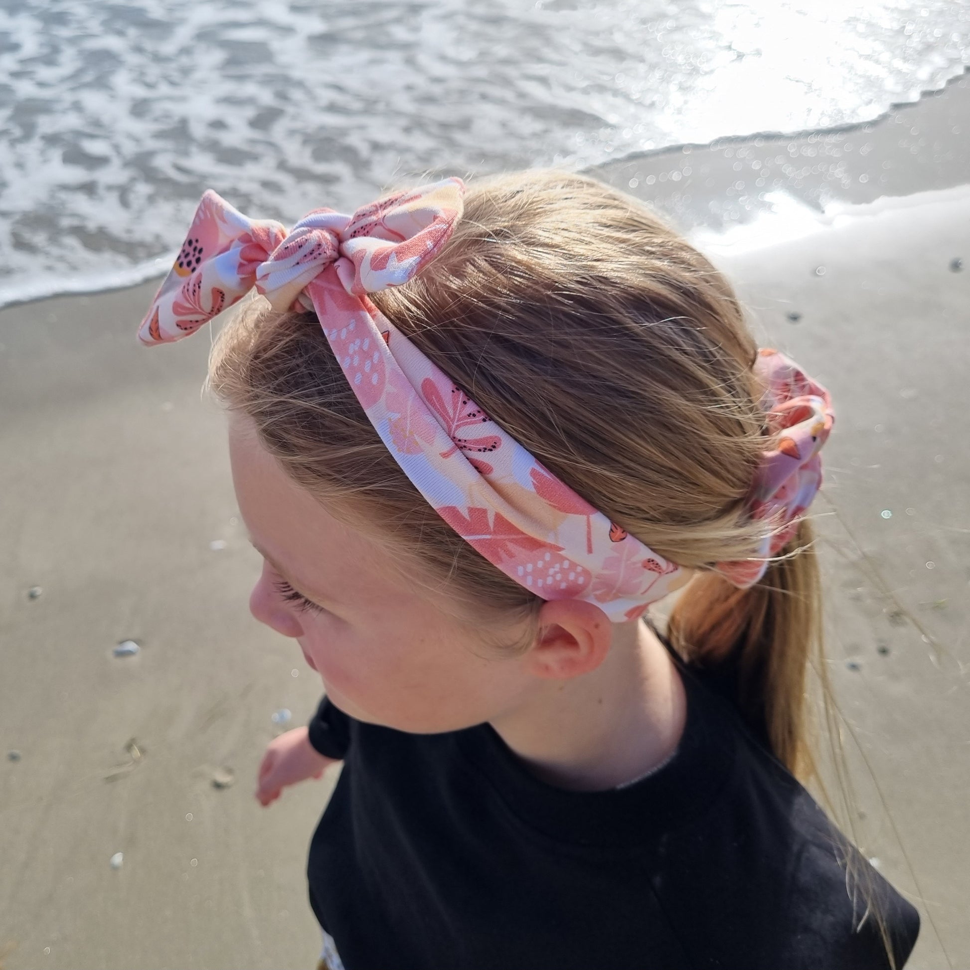 Top Knot Headband - Sara worn by a girl at the beach. Pink and orange leaves on white background. 