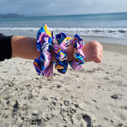 Scrunchie - Swirls on girls wrist at the beach. Blue, orange and purple abstract pattern on pink background.
