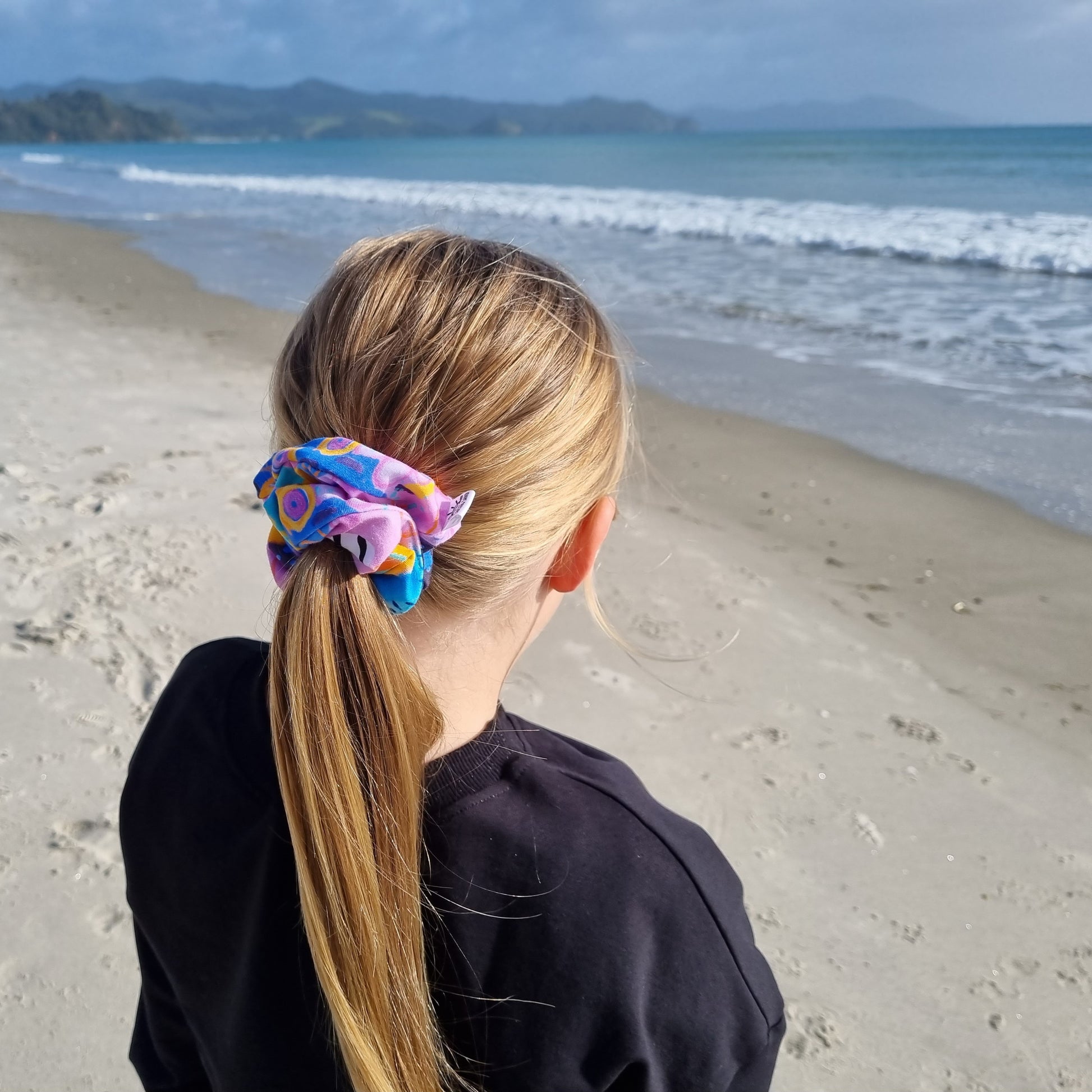 Scrunchie - Swirls tied in girls hair at the beach. Blue, orange and purple abstract pattern on pink background.