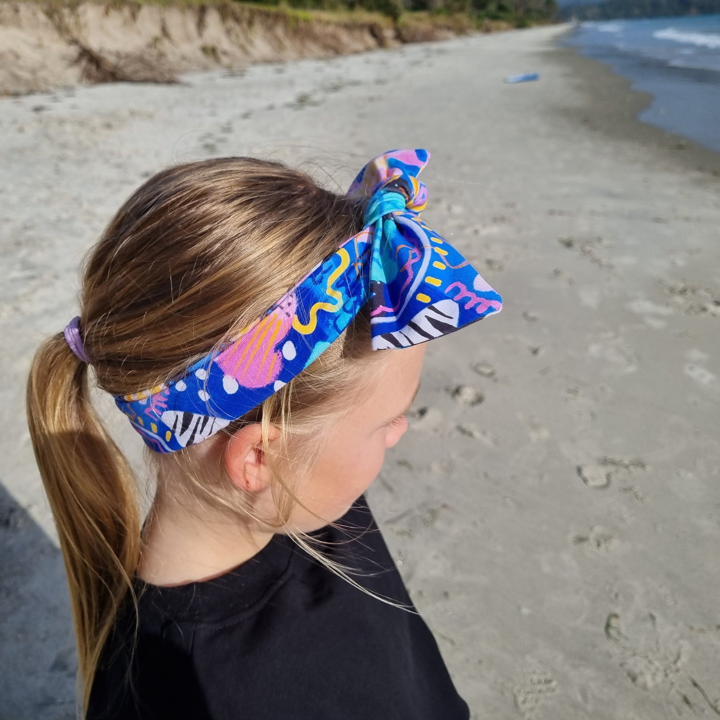 Top Knot Headband - Swirls worn by a girl at the beach. Blue, orange and purple abstract pattern on pink background.