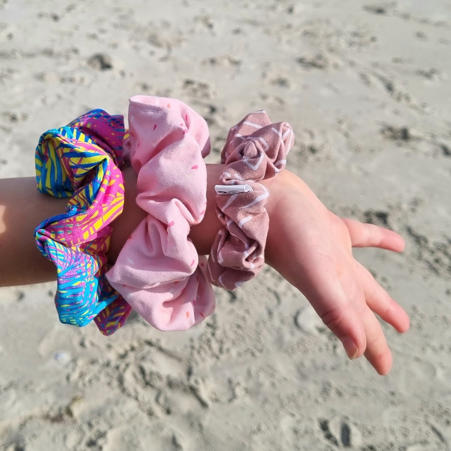 Scrunchie - Pink Sprinkle on girls wrist at the beach. Pink sprinkle design on pink background.