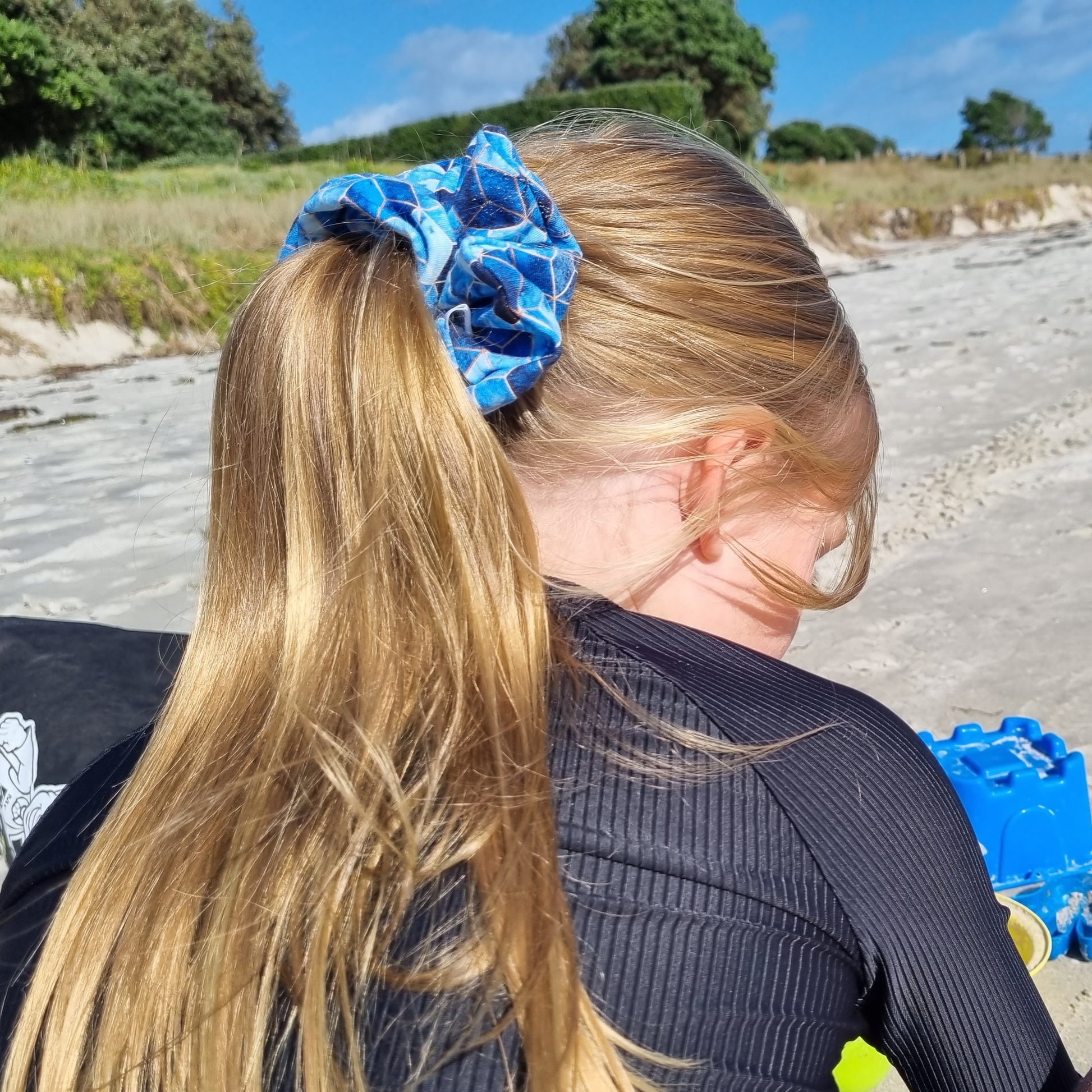 Scrunchie - Geo tied in girls hair at the beach. Gold geometric pattern on mottled blue background.