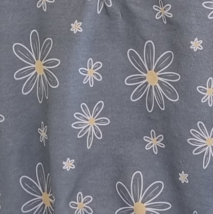 Close-up of Jumper - Sweet Daisy hanging on a wooden rack. White and yellow daisies against soft grey background.