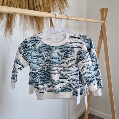 Jumper - Waves hanging on a wooden rack. Sketch design of blue and white waves against white background.