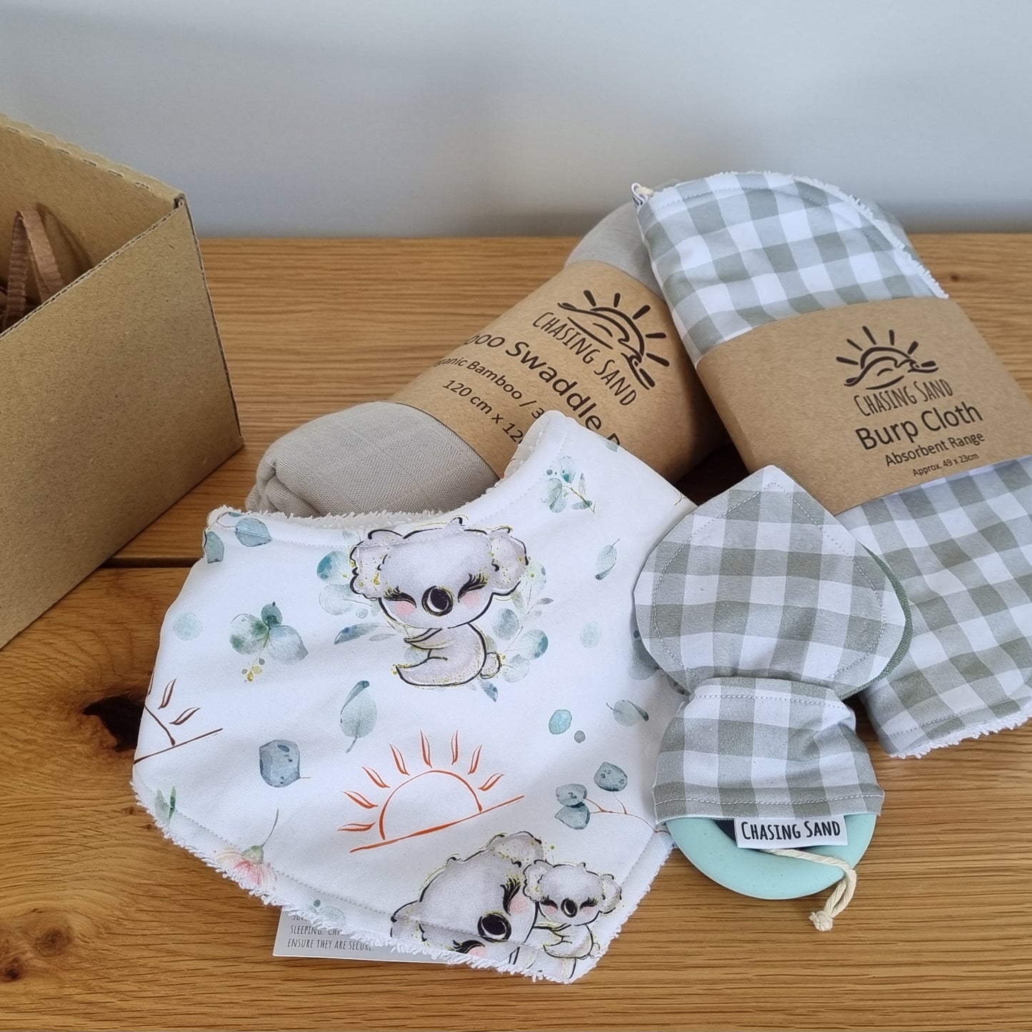 For Baby Gift Box - Neutral against wooden/white backdrop. Each Gift Box contains 1x Swaddle Blanket, 1x Burp Cloth, 1x Dribble Bib and 1x Teether.