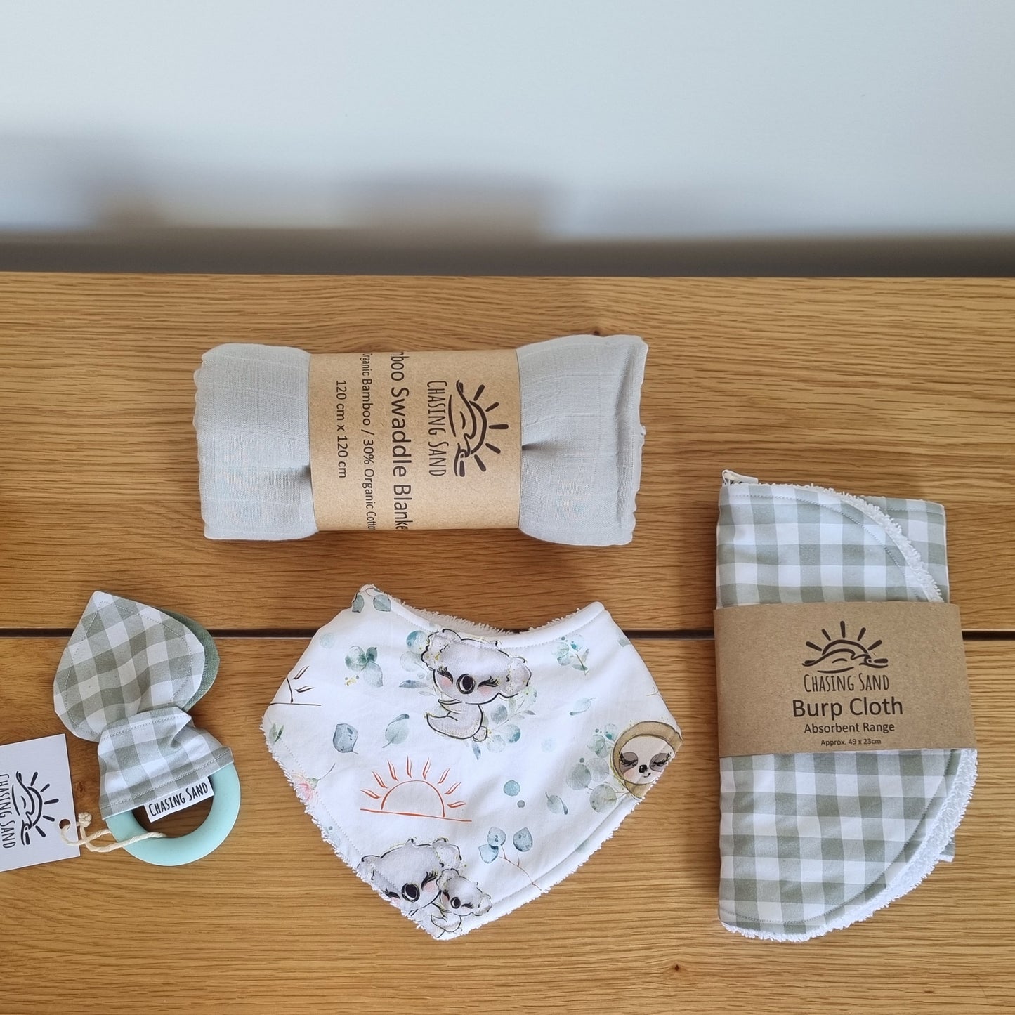 For Baby Gift Box - Neutral against wooden/white backdrop. Each Gift Box contains 1x Swaddle Blanket, 1x Burp Cloth, 1x Dribble Bib and 1x Teether.