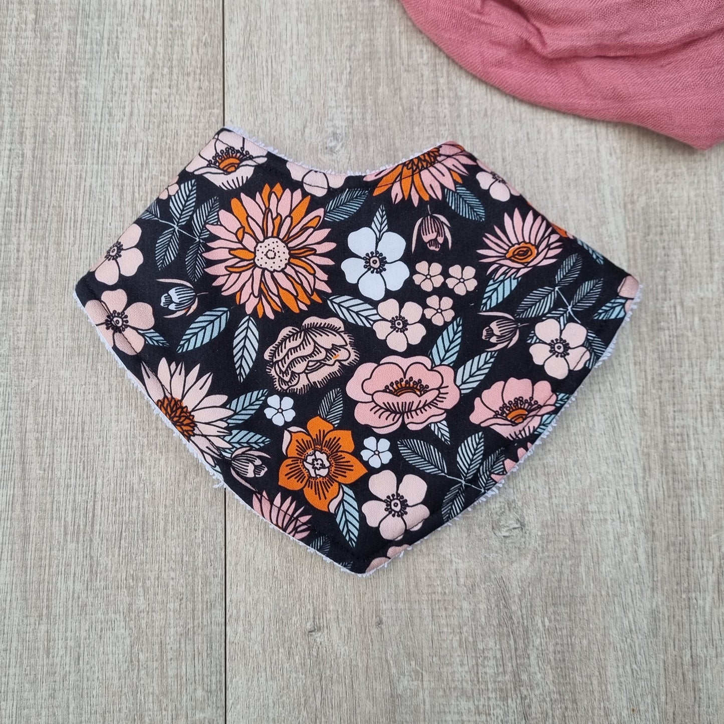 Dribble Bib - Florence against wooden backdrop. Orange and pink flowers with leaves on black background.