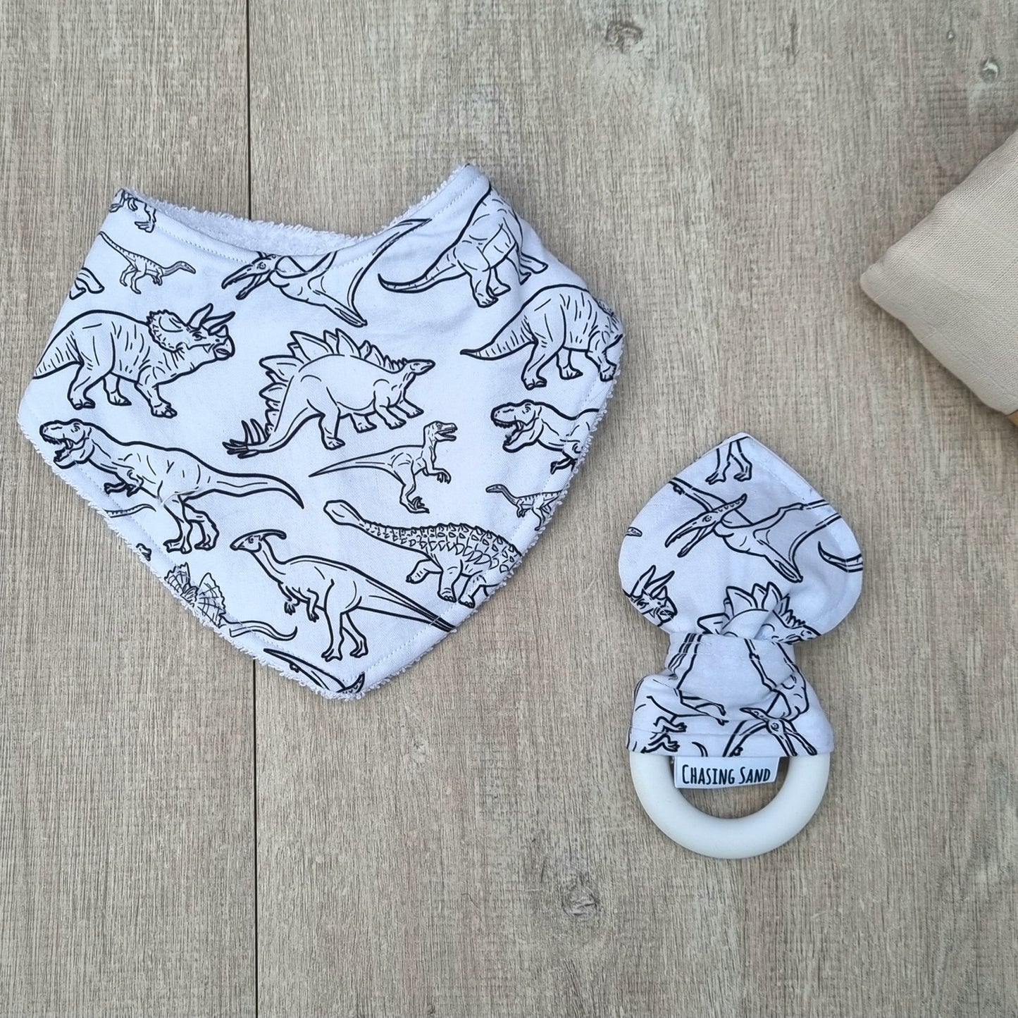 2 Piece Gift Set - B&W Dino against wooden backdrop. Black dinosaur design on white background. Layer bib and matching teether.