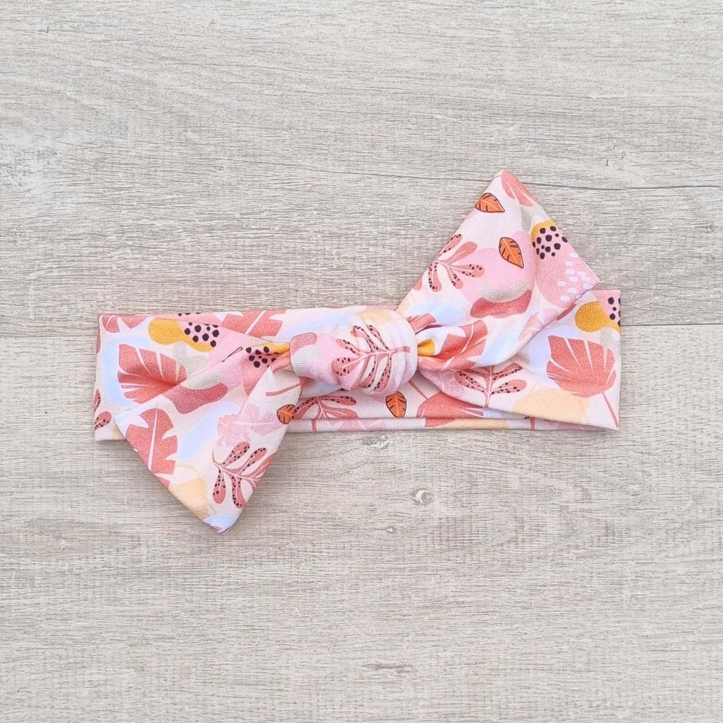 Top Knot Headband - Sara against wooden backdrop. Pink and orange leaves on white background.