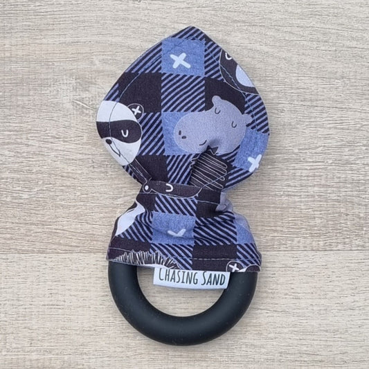 Teether - Night Ninja against wooden backdrop. Hippo and panda illustrations on a black and navy blue gingham background, with black silicone teething ring.