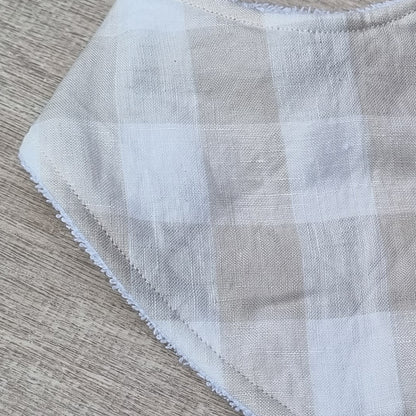 Dribble Bib - Oat Gingham Linen against wooden backdrop. Soft brown checkered pattern on white.